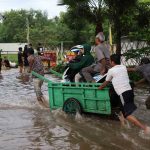 Warga pengguna sepeda motor yang terhadang banjir di Jalan Cileduk Raya, Sabtu, 6 Juli 2024), memanfaatkan jasa perahu gerobak untuk menyeberangi banjir. | Foto: Media Asuransi/Arief Wahyudi
