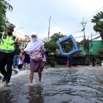 Petugas kepolisian dari Pores Metro Tangerang membantu seorang ibu lansia melewati jalan yang tergenang banjir, di jalan Cileduk Raya, Tangerang beberapa waktu lalu. | Foto: Media Asuransi/Arief Wahyudi