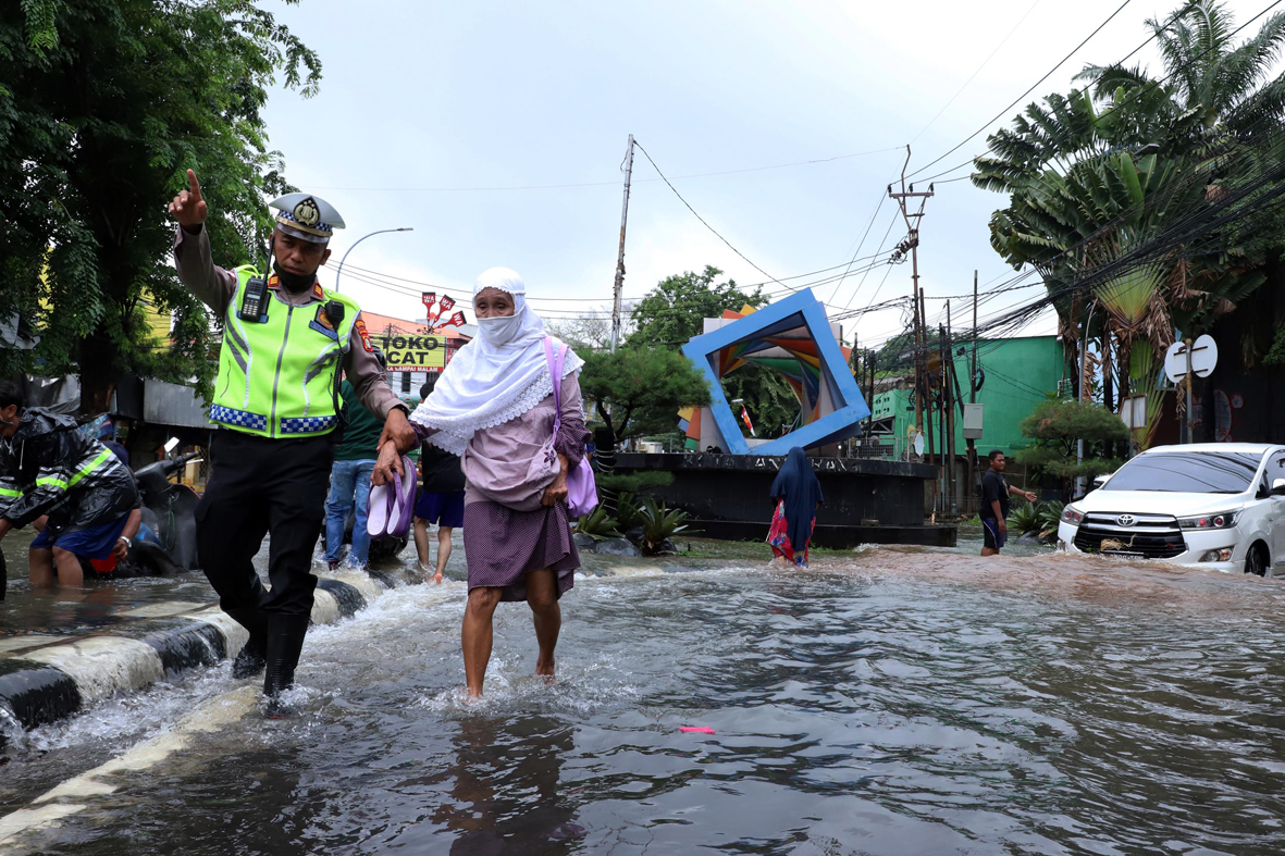 Petugas kepolisian dari Pores Metro Tangerang membantu seorang ibu lansia melewati jalan yang tergenang banjir, di jalan Cileduk Raya, Tangerang beberapa waktu lalu. | Foto: Media Asuransi/Arief Wahyudi