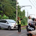 Seorang pekerja sosial atau petugas bayangan (membantu tugas utama penjaga pintu pelintasan kereta api) yang bekerja secara suka rela, sedang membantu mengatur arus lalu lintas di pintu pelintasan kereta api agar tidak terjadi kemacetan dan juga untuk menghindari terjadinya kecelakaan. | Foto: Media Asuransi/Arief Wahyudi