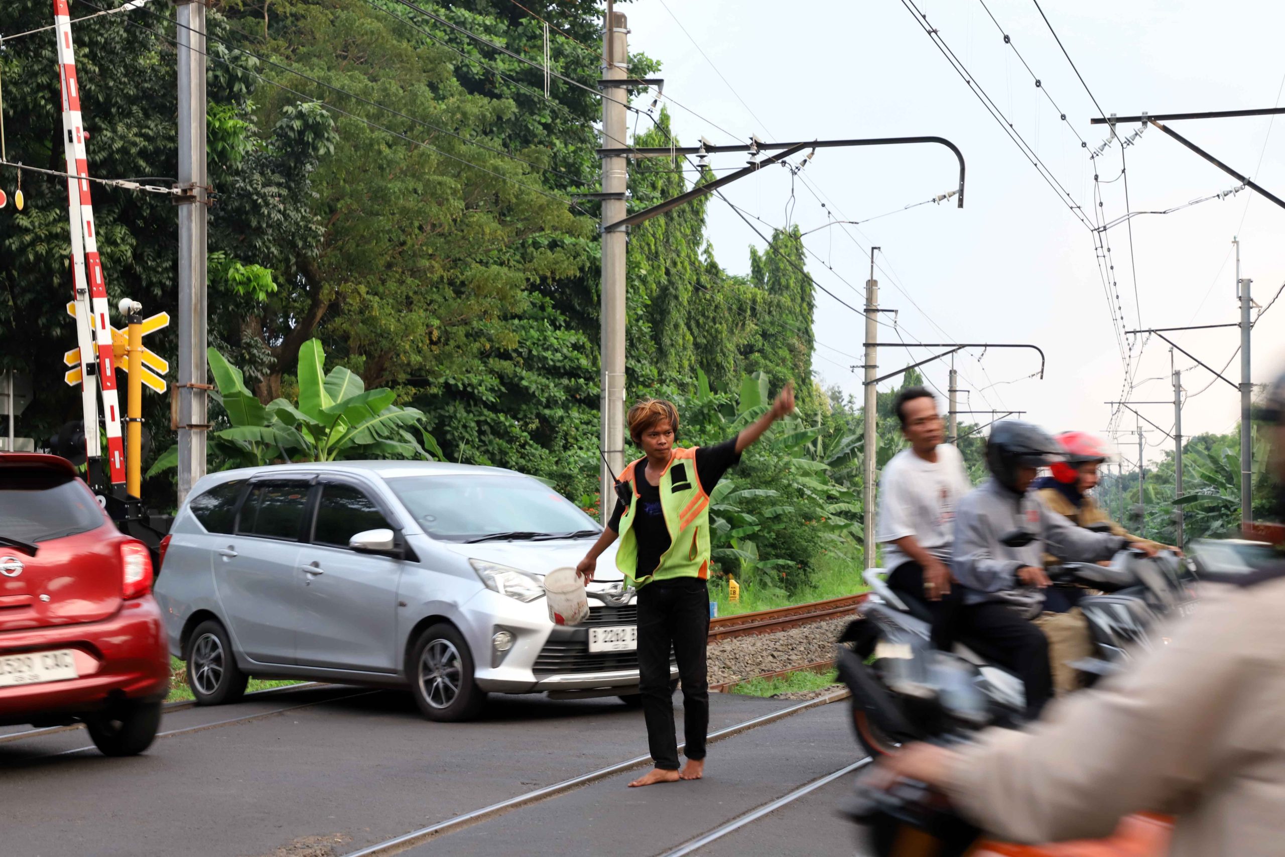 Seorang pekerja sosial atau petugas bayangan (membantu tugas utama penjaga pintu pelintasan kereta api) yang bekerja secara suka rela, sedang membantu mengatur arus lalu lintas di pintu pelintasan kereta api agar tidak terjadi kemacetan dan juga untuk menghindari terjadinya kecelakaan. | Foto: Media Asuransi/Arief Wahyudi
