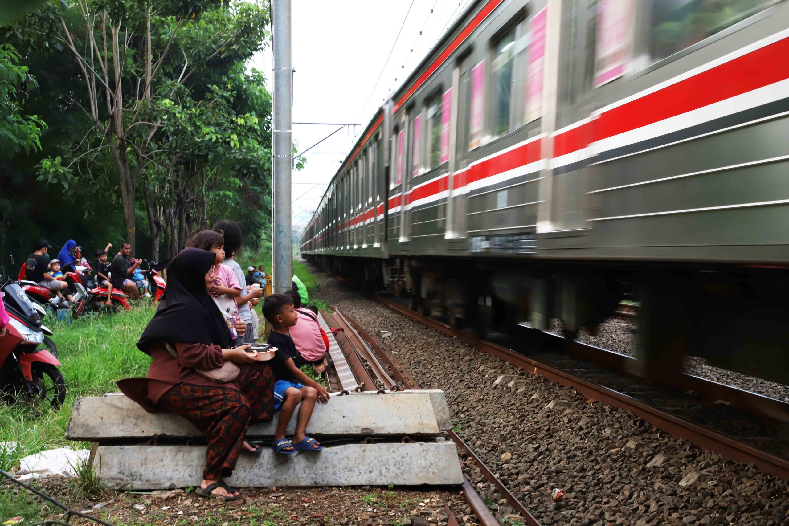 Warga, orang tua dan anak-anak berkumpul di pinggir jalur rel kereta listrik Bintaro menunggu kereta lewat. Meskipun memiliki risiko yang cukup tinggi, banyak orang tua yang kerap mengajak anaknya untuk datang ke lokasi tersebut  saat sore hari sebagai sarana hiburan anak-anak mengisi waktu liburan sekolah. | Foto: Media Asuransi/Arief Wahyudi