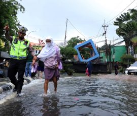 Petugas kepolisian dari Pores Metro Tangerang membantu seorang ibu lansia melewati jalan yang tergenang banjir, di jalan Cileduk Raya, Tangerang beberapa waktu lalu. | Foto: Media Asuransi/Arief Wahyudi