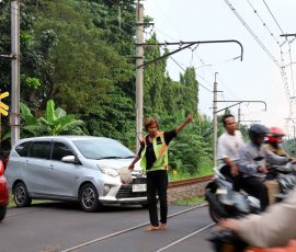 Seorang pekerja sosial atau petugas bayangan (membantu tugas utama penjaga pintu pelintasan kereta api) yang bekerja secara suka rela, sedang membantu mengatur arus lalu lintas di pintu pelintasan kereta api agar tidak terjadi kemacetan dan juga untuk menghindari terjadinya kecelakaan. | Foto: Media Asuransi/Arief Wahyudi